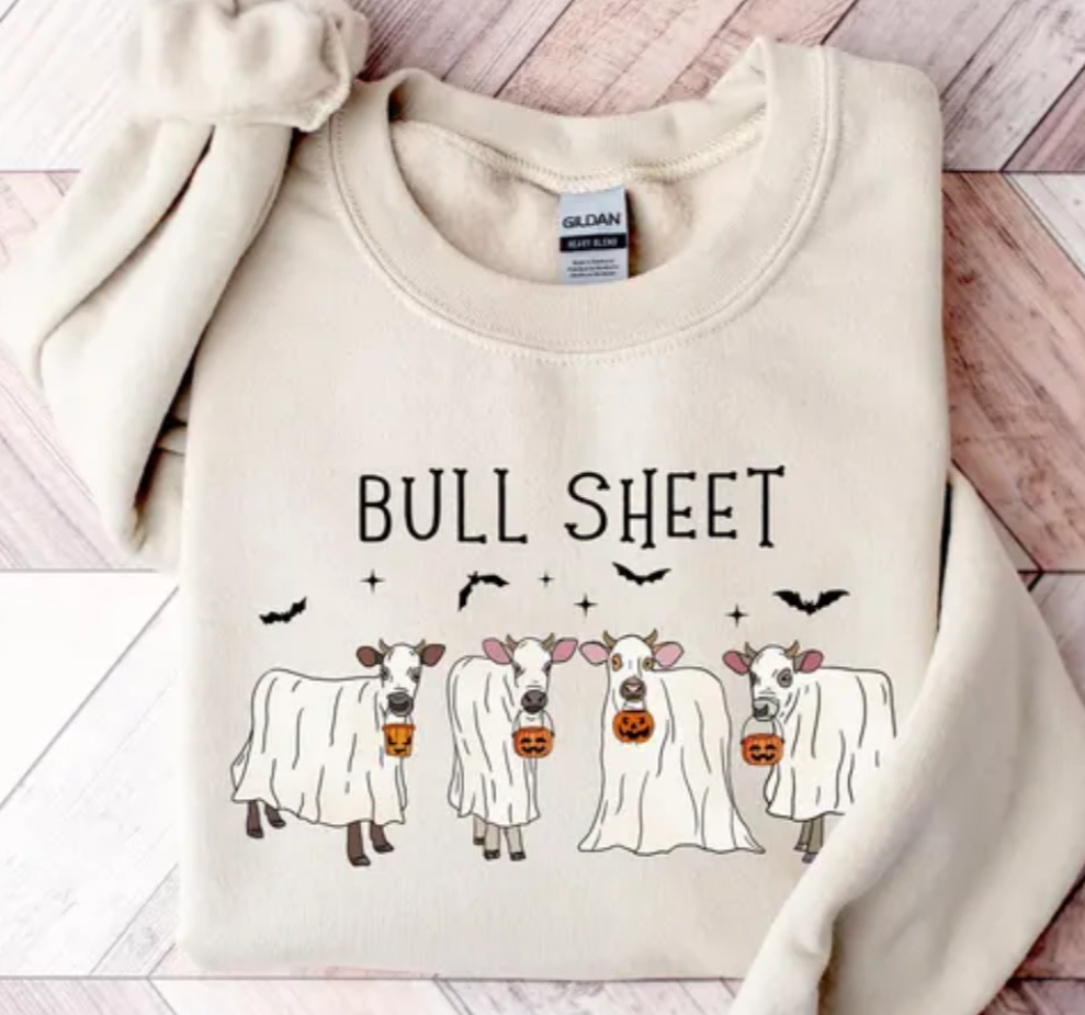 Beige sweatshirt with 'Bull Sheet' text and cow illustrations on a wooden surface